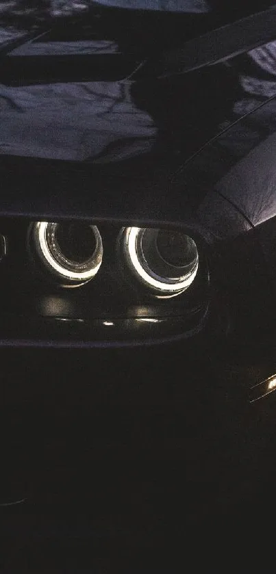Sleek black car in dark setting with illuminated headlights.