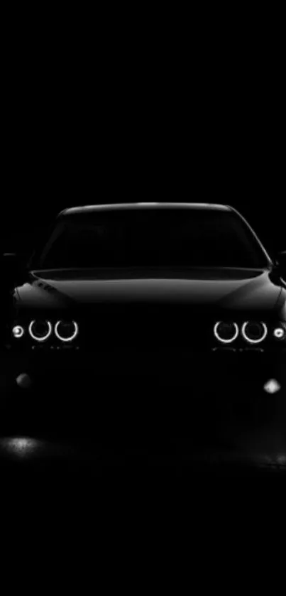 Sleek black car with glowing headlights in dark background.