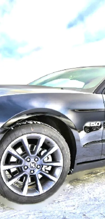 Sleek black car with shiny wheels on a snowy road, under a clear sky.