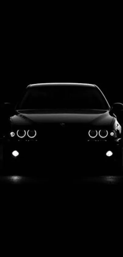 Front view of a sleek black car with glowing headlights in the dark.