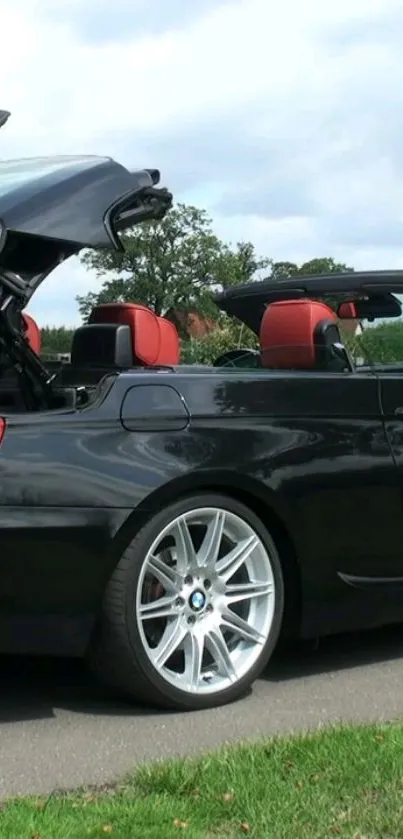 Black convertible car with red seats on a scenic road.