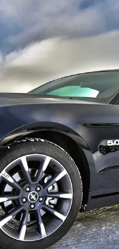 Sleek black sports car with chrome wheels and cloudy sky.