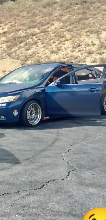 Blue car with spoiler on a mountainside road, perfect for car enthusiasts.