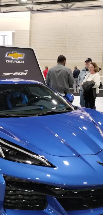 Blue sports car displayed at an auto show with people around.