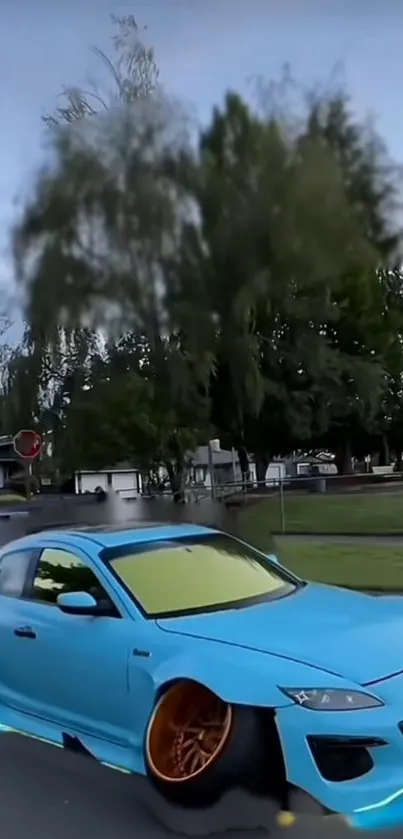 Blue sports car parked on urban street with trees in background.