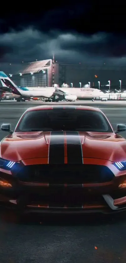 Red car at airport with plane in background at night.