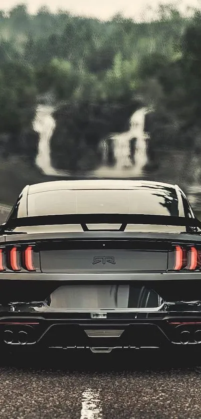 Sleek black car with a waterfall in the background, captured on a scenic road.