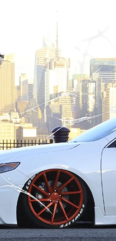 White car with red wheels in front of a city skyline at sunset.