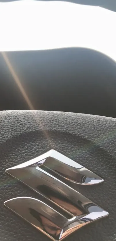 Chrome car logo on a textured steering wheel in sunlight.