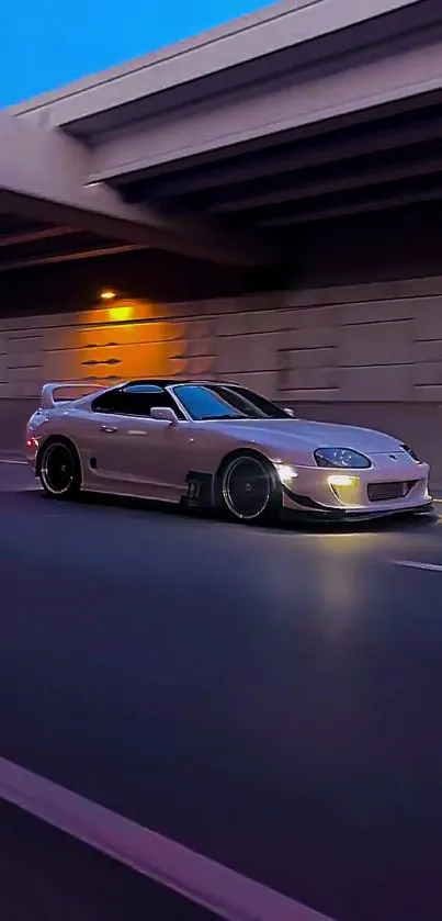 A sleek sports car driving down a city road at night with a vivid blue sky.