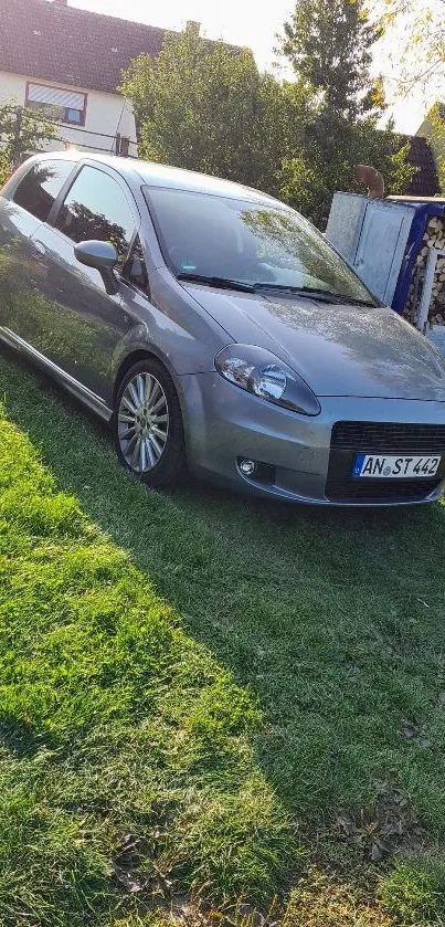 Silver car parked on vibrant green grass under sunlight.