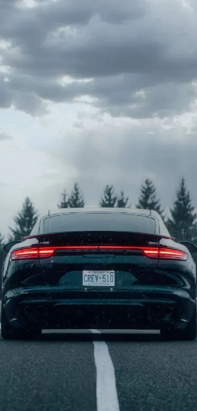 Sleek car with glowing tail lights on an expansive road under a dramatic sky.