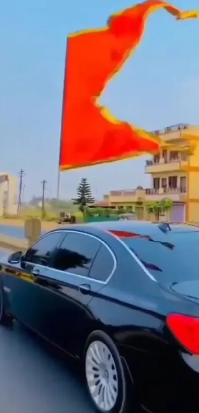 Black car driving with a red flag on urban street.