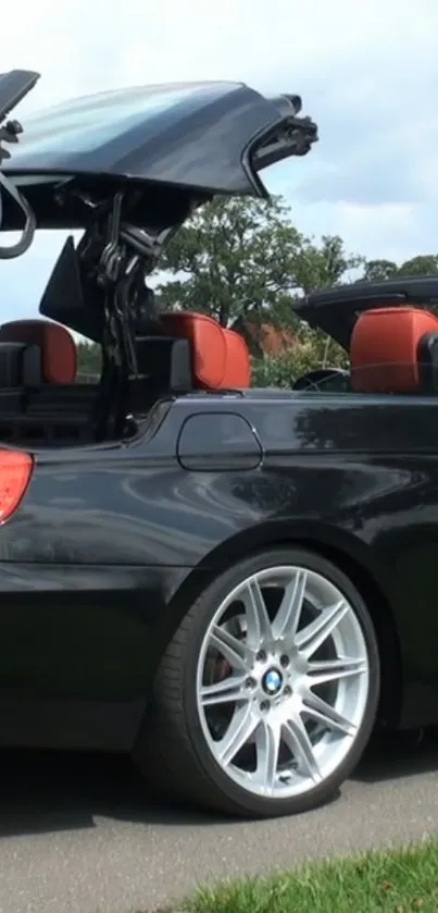 Sleek black convertible car with open roof on a road.