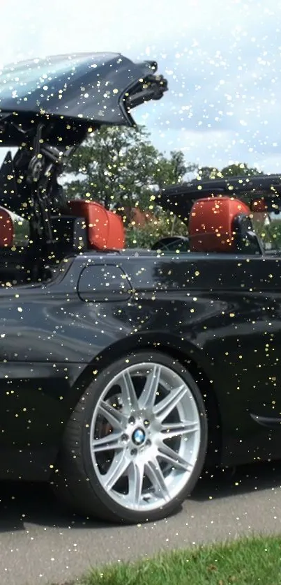 Black convertible car with open top and golden sparkles on the road.