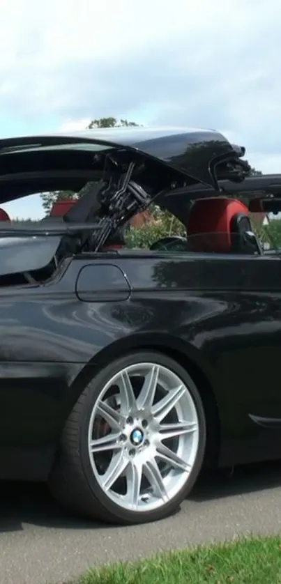 Black convertible car with red interior against a cloudy sky backdrop.