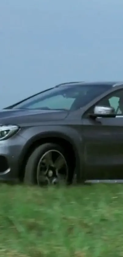 Sleek grey car driving on a grassy field under blue sky.