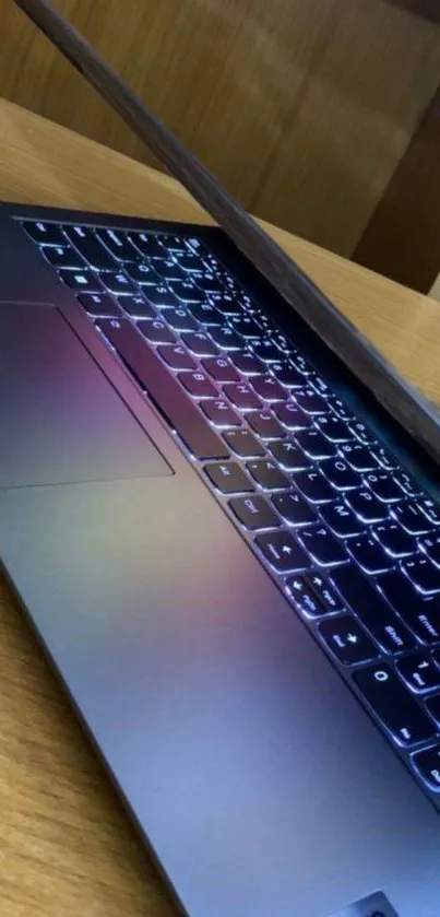 Sleek laptop half-closed on wooden desk with illuminated keyboard.