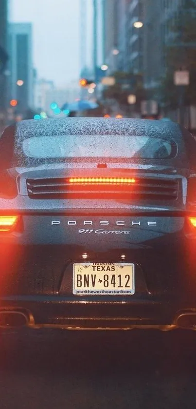 Back view of Porsche Carrera in city at night with red tail lights.