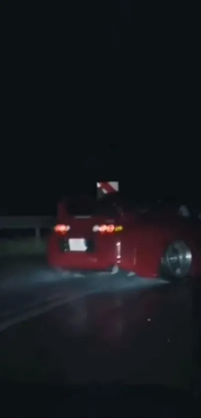 Red car driving on a dark road at night.