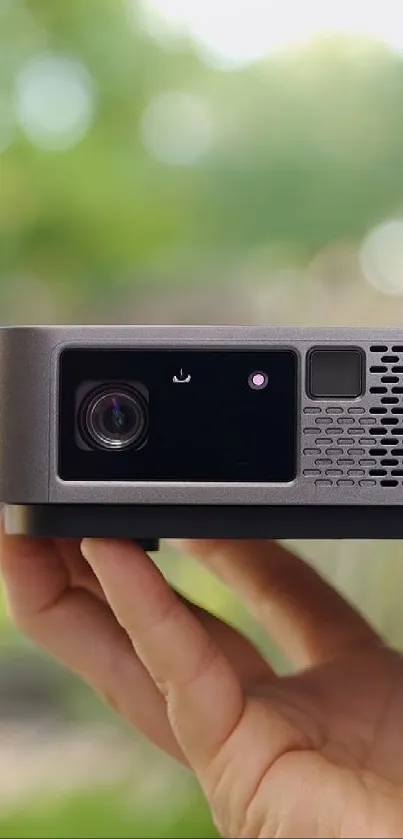 Hand holding a sleek portable projector for outdoor use.