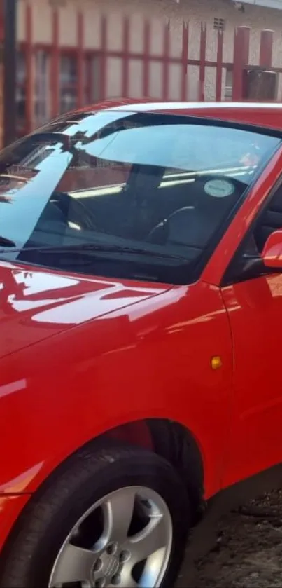 Red car parked near a red fence, shining in sunlight.