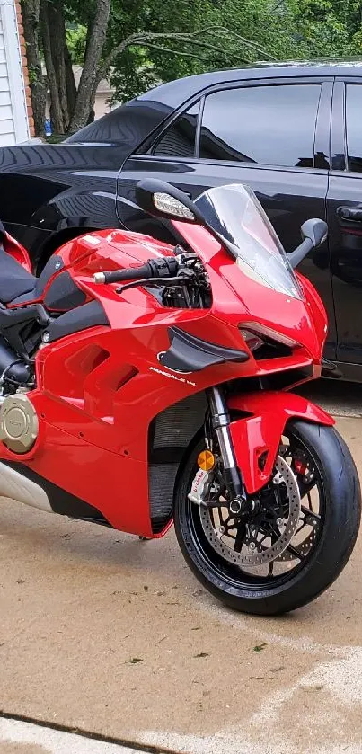 Sleek red motorcycle in driveway with black car.