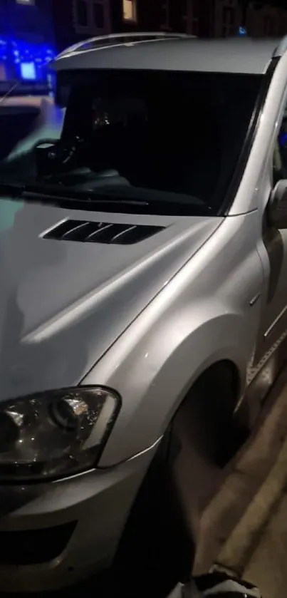 Sleek silver car parked under city lights at night.