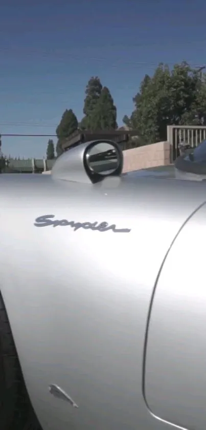 Sleek silver Spyder car side view with blue sky backdrop.