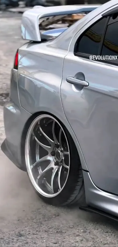 Sleek silver sportscar with shiny wheels on a textured surface.