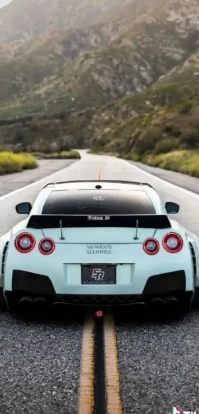 Sports car on a scenic open road with mountainous background.