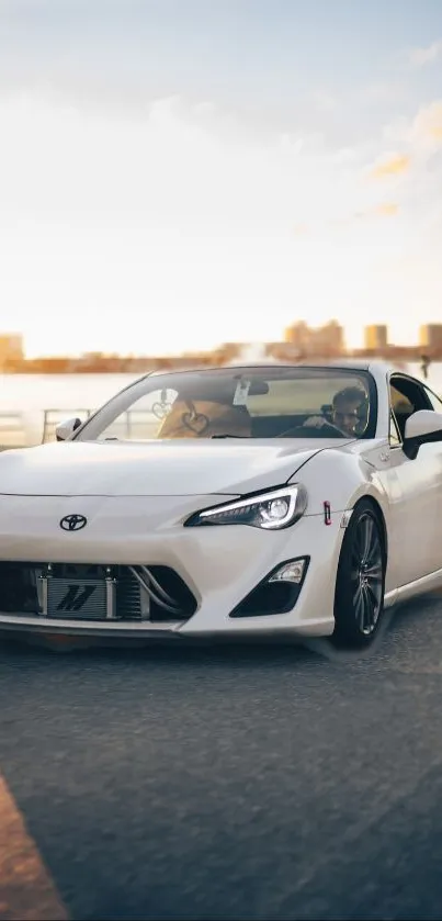 White sports car driving at sunset with city skyline.