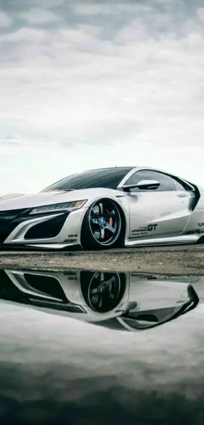 Sleek sports car reflecting in a puddle under a cloudy sky.