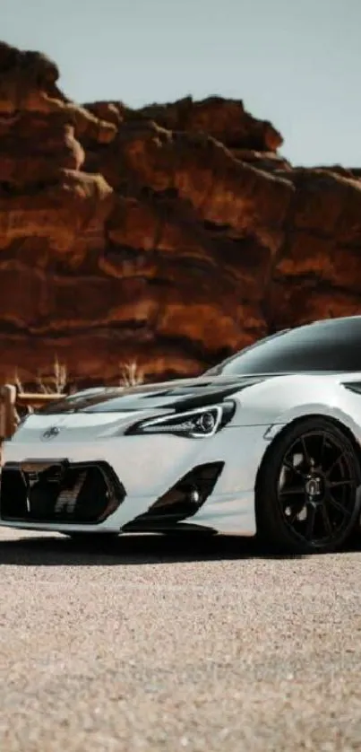 Sleek sports car with rocky background under clear sky.