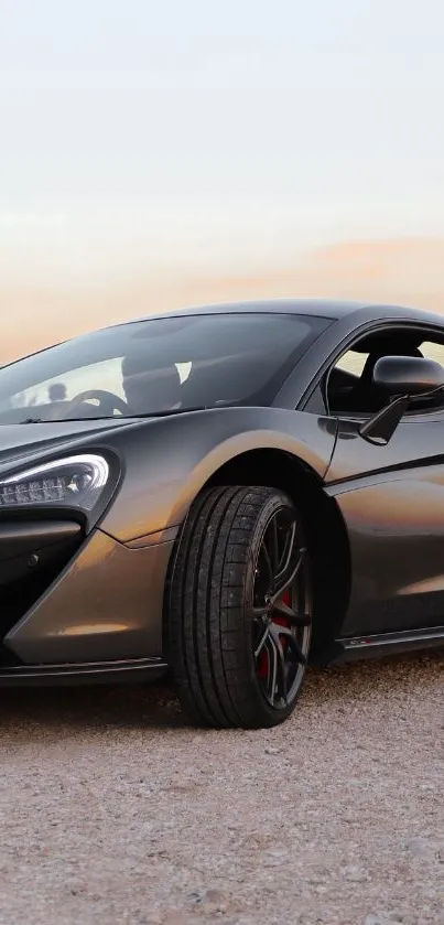 Sleek gray sports car on a gravel road at sunset.