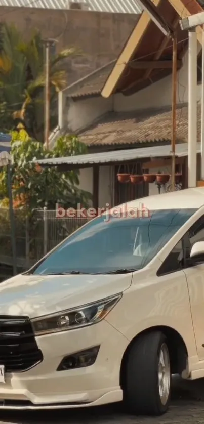 White car on a rustic urban street with trees and a modern house in the background.