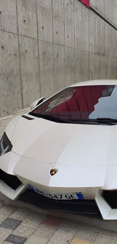 Sleek white supercar in urban setting with concrete wall backdrop.