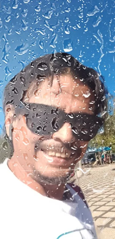 Smiling man behind raindrop-covered glass outdoors.