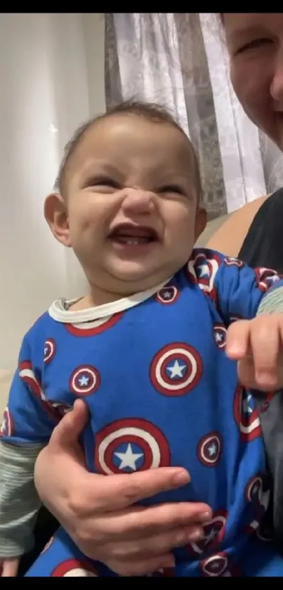 Smiling baby wearing a blue onesie with playful patterns.