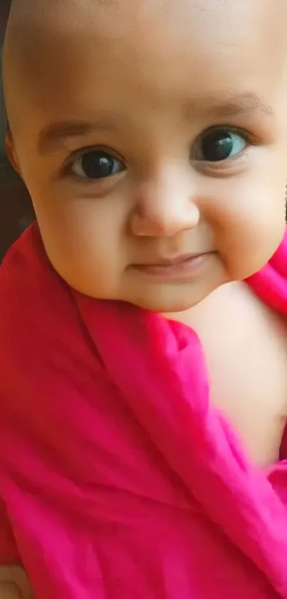 Smiling baby wrapped in a vibrant pink blanket on mobile wallpaper.