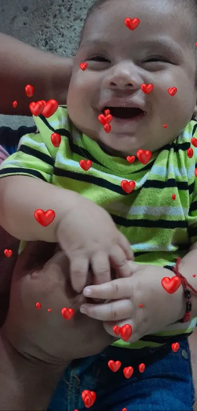 Smiling baby wearing a green striped shirt, being held lovingly.