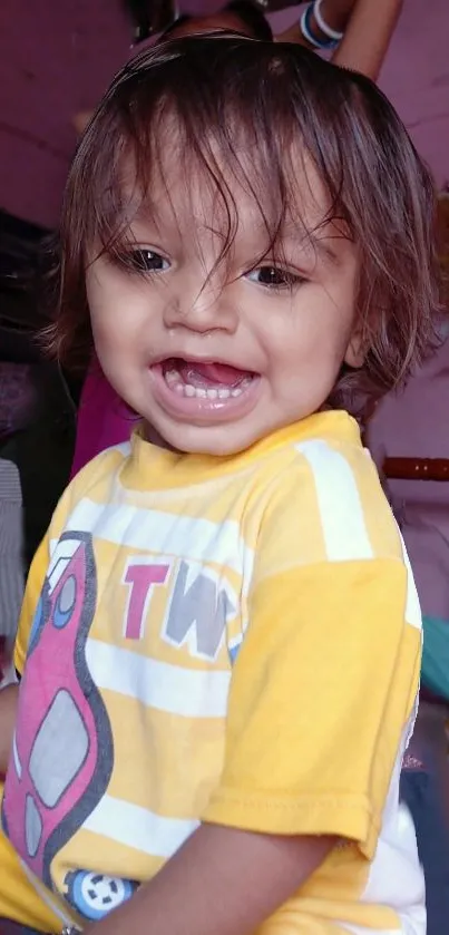 Smiling baby with brown hair, wearing a yellow shirt.