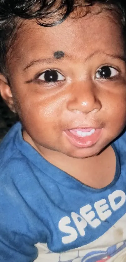 Smiling baby with a blue shirt in natural lighting.