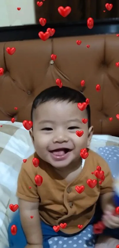 Smiling baby with red heart overlay on a brown sofa.