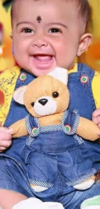 Happy baby in overalls with a teddy bear, smiling brightly.