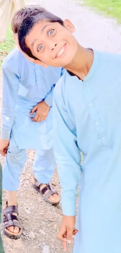 Boy in light blue clothing smiling brightly outdoors.