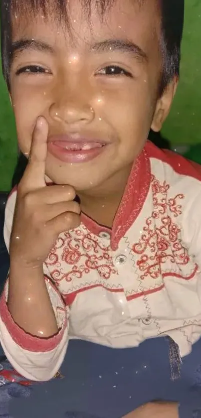 A joyful boy in a traditional outfit smiles with a green background.