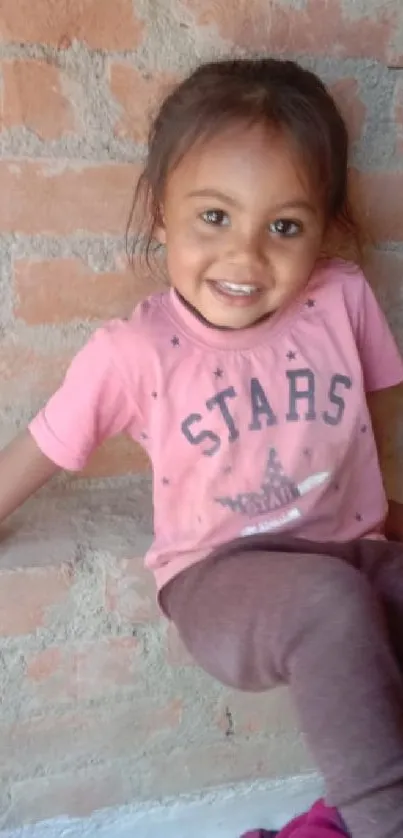 Adorable child smiles against a brick wall.