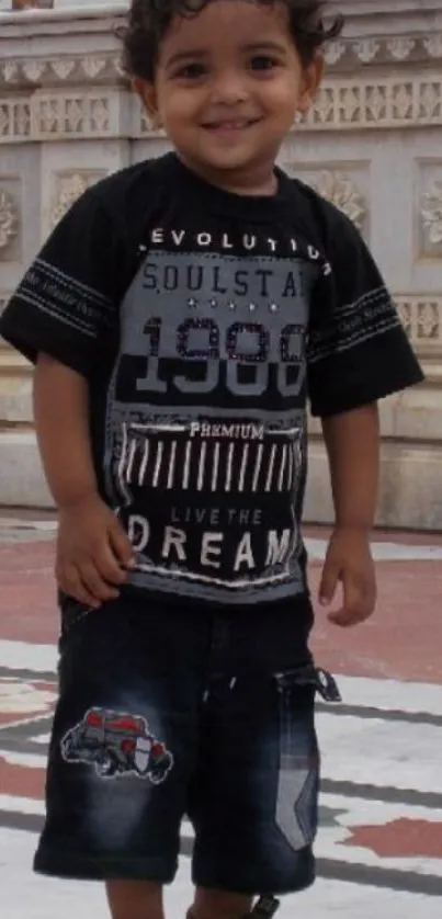 Smiling child stands by an ornate wall.