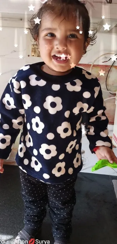 Smiling child in black and white flower sweater, standing indoors.